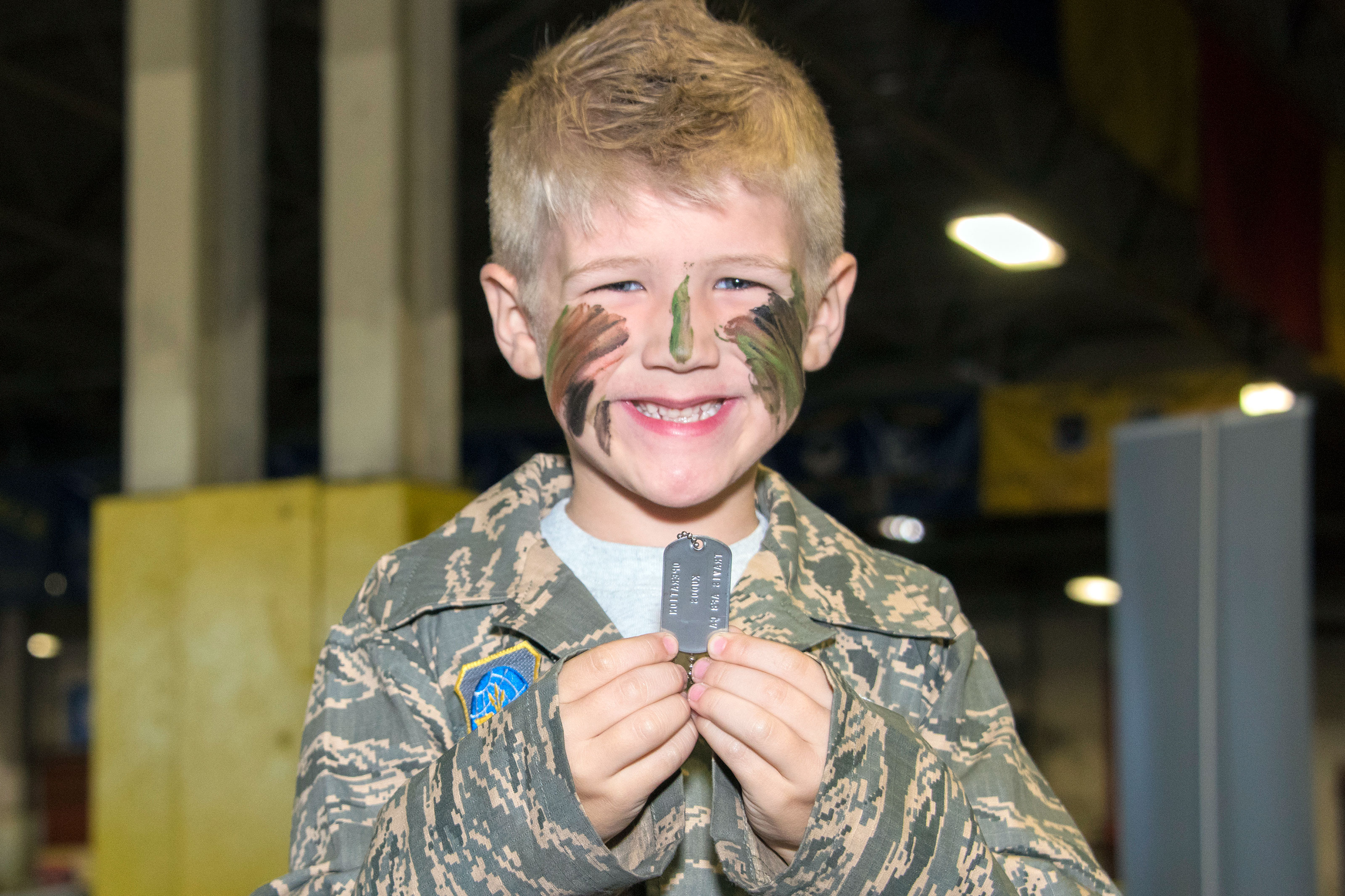 A child displays the dog tags he received as part the out-processing line at the 60th Aerial Port Squadron cargo warehouse, set up to host U. S. Air Force families for Kids Understanding Deployment Operations day, Oct. 21, 2017, Travis Air Force Base Calif. (U.S. Air Force/Heide Couch)