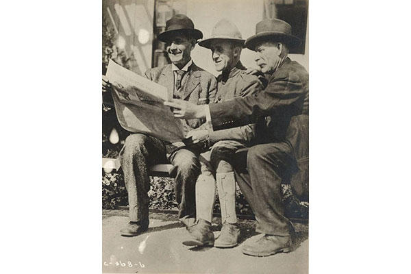 A father, son, and uncle share a newspaper on a visitor's day during training camp. (Photo: National Archives and Records Administration)