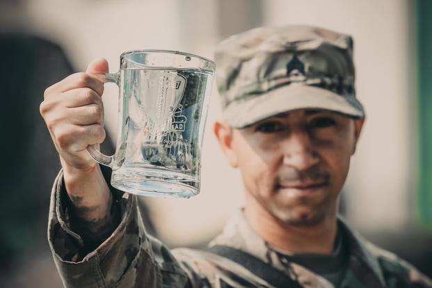 Sgt. Daniel Baudoin, a water purification specialist with the 240th Composite Supply Company of Baumholder, Germany, proudly displays his battalion crest June 2, 2018 which contains freshly purified water he and his team produced. (Michigan Army National Guard/Spc. Aaron Good)
