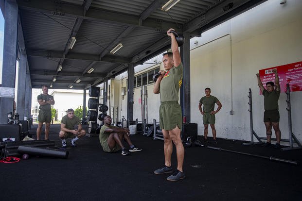 A Marine performs a military press with kettlebells.