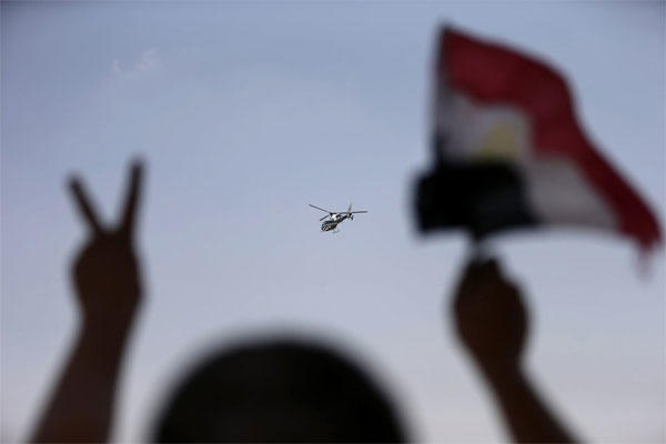 A police helicopter flies over the presidential palace, as a man waves the Egyptian national flag , in Cairo, Egypt, Tuesday, July 2, 2013.