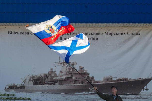 A pro-Russian activist waves the Russian state, upper, and Russian Navy flags outside an entrance to the General Staff Headquarters of the Ukrainian Navy in Sevastopol, Ukraine, Monday, March 3, 2014. (AP Photo/Andrew Lubimov)