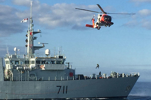 An aviation survival technician and a public affairs specialist were lowered onto the Canadian Warship HMCS Summerside for a mock medical evacuation. (U.S. Coast Guard)