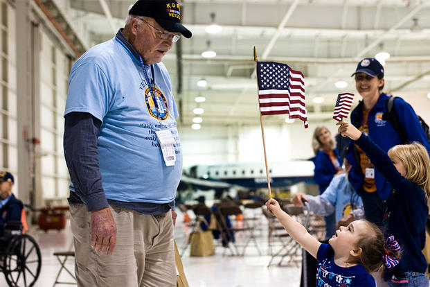 A child presents a U.S. flag to a Korean War veteran at Denver International Airport. 