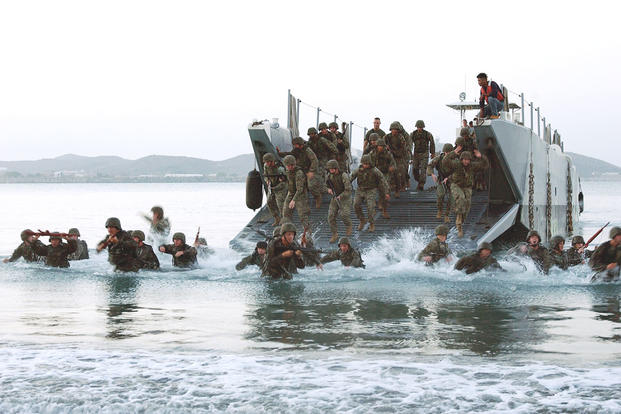 U.S. Marines and sailors assigned to the 1st Fleet Antiterrorism Security Team, 7th Platoon, jump out of their landing craft during a pre-dawn amphibious assault exercise.