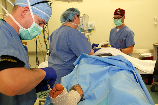R.N. Valerie Haddle and Capt. Christopher Renaud, the anesthesiologist, check the patient's vital signs as Nurse Technician Sgt. Robert Larkin finishes wrapping the foot on which they have just operated. (U.S. Army/Rachael Tolliver)
