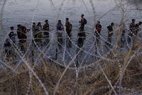 Migrants wait to climb over concertina wire after they crossed the Rio Grande and entered the U.S. from Mexico
