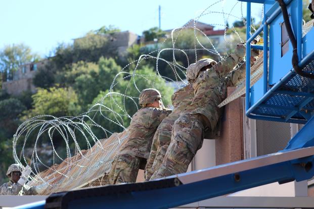 Soldiers add concertina wire to the top of the Arizona-Mexico border wall.