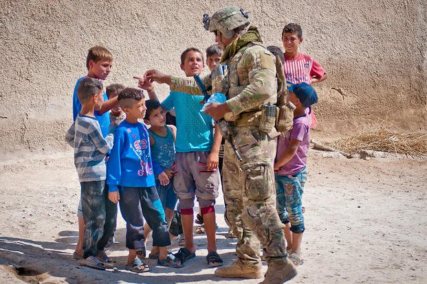 A soldier hands out candy to a group of kids during a patrol along the demarcation line outside Manbij, Syria, July 14, 2018. Army photo by Staff Sgt. Timothy R. Koster