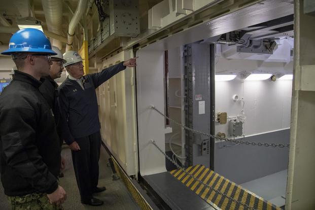 Secretary of the Navy Richard V. Spencer is briefed by Lt. Cmdr. Chabonnie Alexander, USS Gerald R. Ford’s ordnance handling officer, on the advanced weapons elevator during a tour of the carrier, Jan. 17, 2018. (U.S. Navy/Mass Communication Specialist 2nd Class Kiana A. Raines)