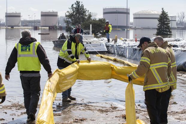 Contracted employees of the Environmental Restoration, LLC company, along with Offutt Air Force Base firefighters, deploy a spill containment boom March 18, 2019 around the Offutt Air Force Base fuel storage area as a precautionary measure following flooding. (U.S. Air Force/Delanie Stafford)