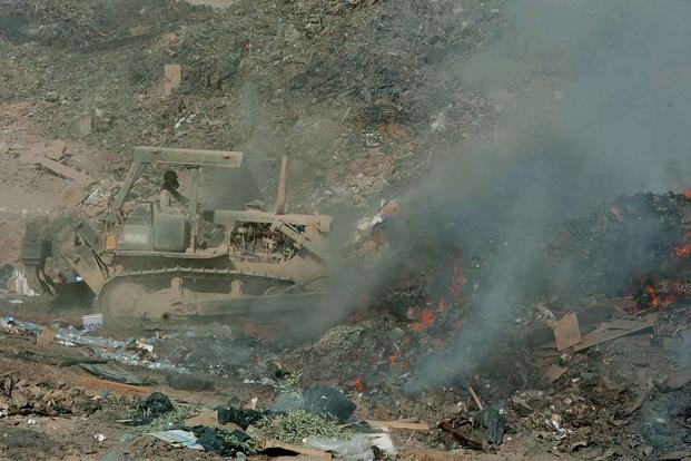 A soldier uses a bulldozer to maneuver refuse into the burn pit in Balad, Iraq, in September 2004.