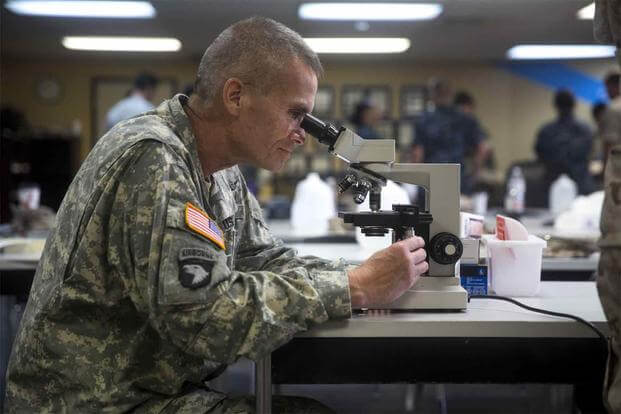 A soldier examines a blood sample in a microscope.