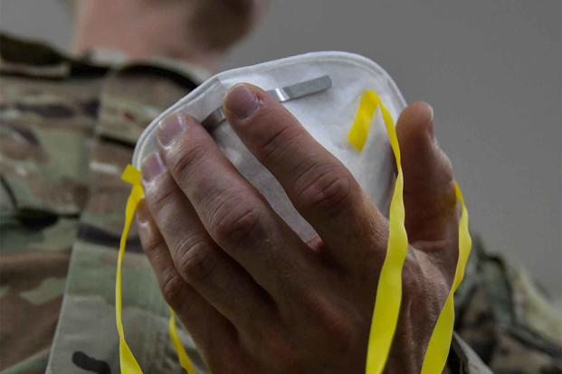 An airman adjusts the straps to his N95 mask.