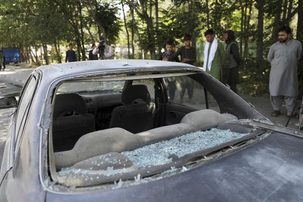 Afghan men look at a damaged car after a roadside bomb explosion in Kabul, Afghanistan