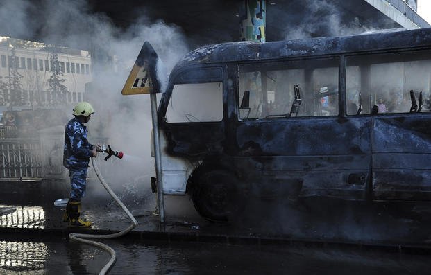 Syrian firefighter extinguishes a burned bus at the site of a deadly explosion, in Damascus, Syria