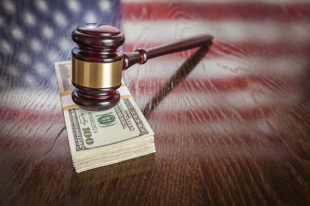 Gavel of justice coming down on pile of cash against blurred background featuring Old Glory