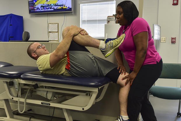 A physical therapy assistant stretches an airman's quadriceps.