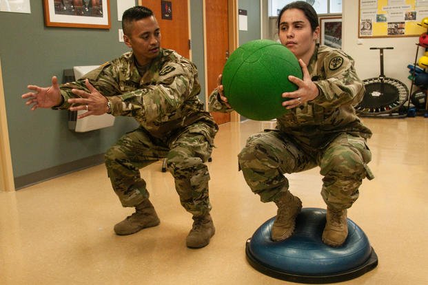 An Army physical therapist shows a patient how to perform a stability ball exercise properly.