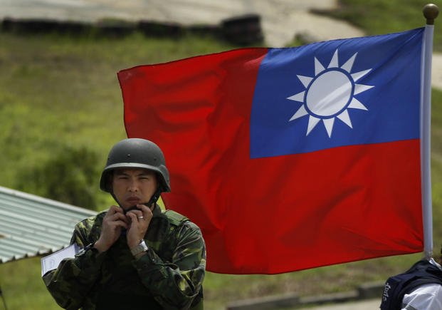 A Taiwan soldier adjusts his helmet in front of a Taiwan flag.