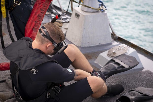 A sailor dons swim fins during a man overboard drill.