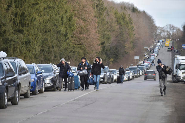 Ukrainians walk past a queue of cars heading to the Poland border 