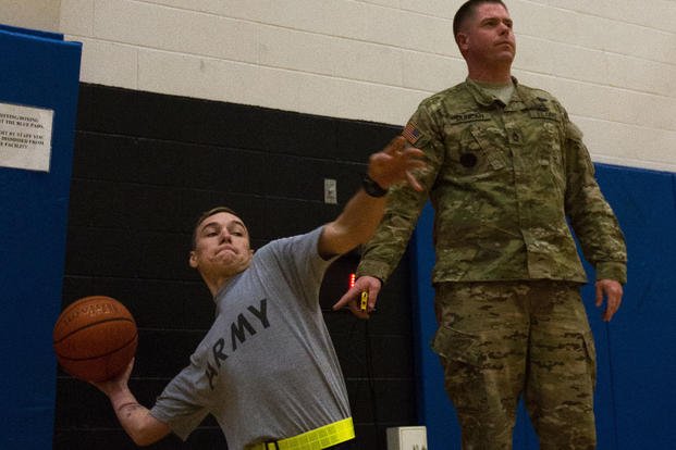 An infantryman throws a basketball from a kneeling position as part of a candidate fitness assessment.