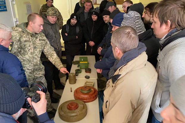 An officer points to the pieces of a disassembled mine in Ukraine.