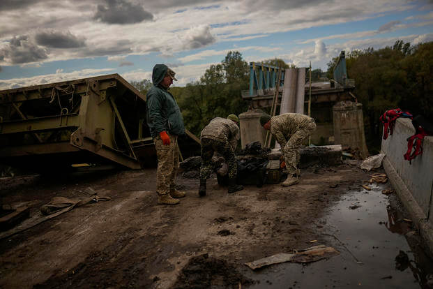 Ukrainian soldiers remove metal pieces as they work on a bridge damaged during fighting with Russian troops in Izium, Ukraine.