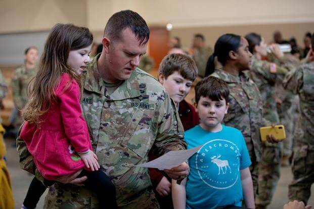 A soldier looks at paperwork while reuniting with his family.