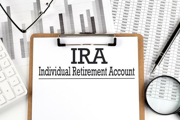 A stock image of a paper on a clipboard reading "IRA" and "Individual Retirement Account" on a table with other papers.
