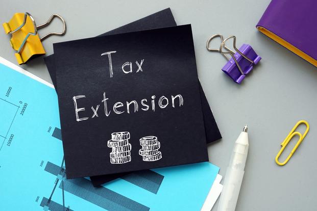 a sticky note with the words "tax extension" surrounded by office supplies
