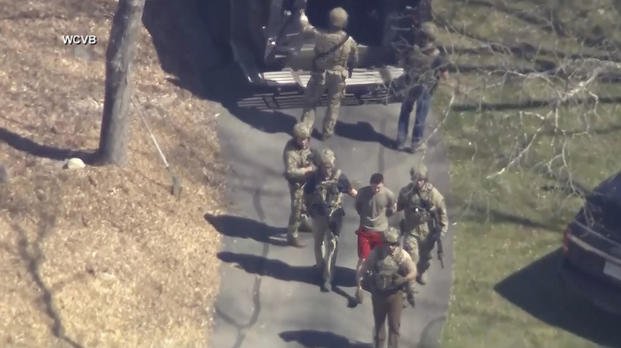 Jack Teixeira, in T-shirt and shorts, being taken into custody by armed tactical agents