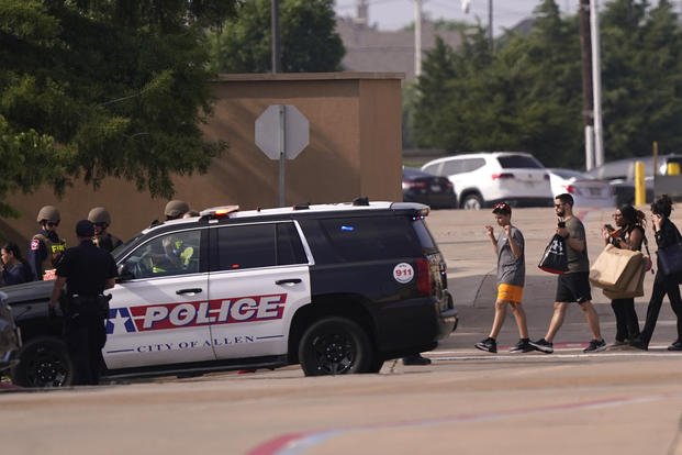 People raise their hands as they leave a shopping center after a shooting in Allen, Texas.