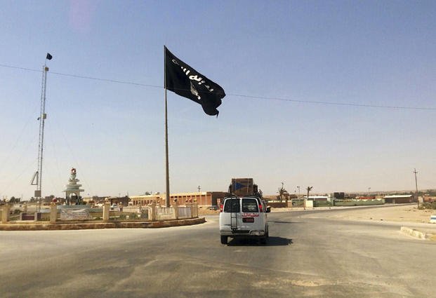 vehicle passes by a flag of the Islamic State group in central Rawah, Iraq