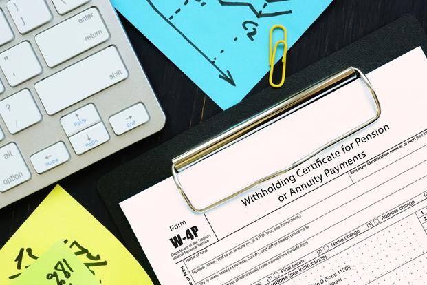 An IRS Form W-4P, miscellaneous office supplies and a computer keyboard are arranged on a surface