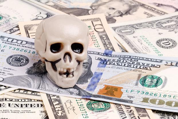 A miniature smiling skull sits on a pile of US cash