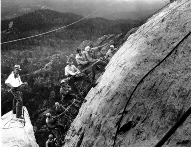 Sculptor Gutzon Borglum directs the carving from a projecting ledge at the left as drillers, suspended in slings fastened with cables to the winches at the top of the mountain, work on George Washington’s head of the Mount Rushmore Memorial in the Black Hills area of Keystone, S.D.