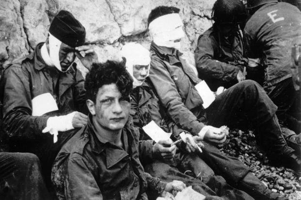 Men of the American assault troops of the 16th Infantry Regiment, injured while storming a coastal area code-named Omaha Beach during the Allied invasion of the Normandy, wait by the chalk cliffs at Collville-sur-Mer for evacuation to a field hospital on D-Day.