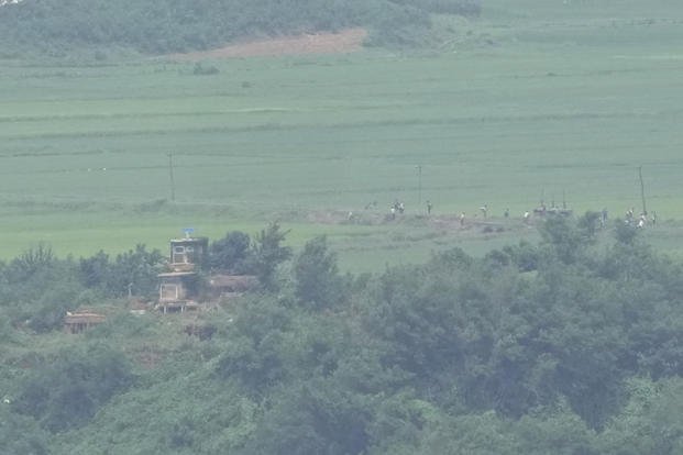 North Koreans work on a field near a North Korean military guard post