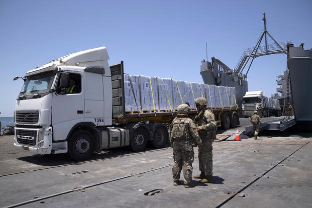 Army soldiers stand next to trucks loaded with humanitarian aid.