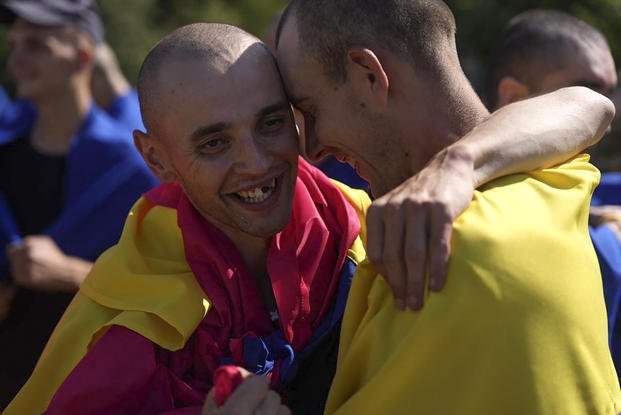 Ukrainian prisoners of war wrapped in national flags hug each other.