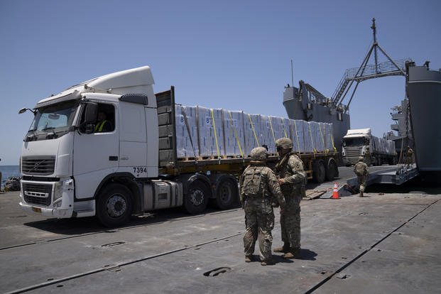 U.S. Army soldiers stand next to trucks arriving loaded with humanitarian aid at the U.S.-built floating pier Trident