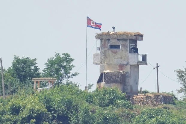 A soldier stands at a North Korean military guard post flying a national flag.