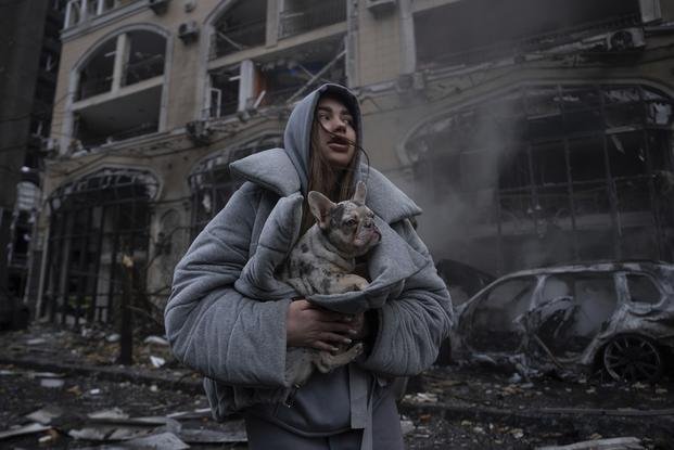 Ivanna, warms her dog in front of a destroyed burning car after a recent Russian attack in Kyiv