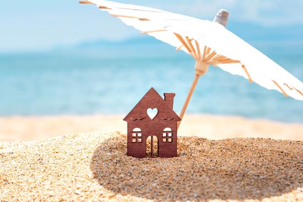 house cutout under paper umbrella in sand