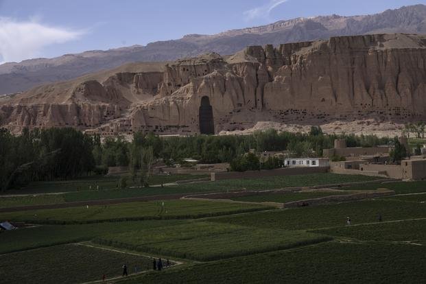 Villagers walk in the fields near the niche of the giant Buddha statue destroyed by the Taliban in 2001, in Bamiyan, Afghanistan
