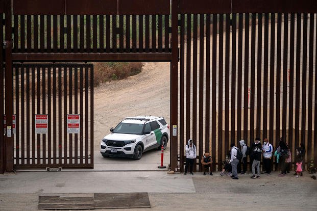 Migrants and asylum seekers wait to be processed by the Border Patrol between fences at the U.S.- Mexico border seen from Tijuana, Mexico