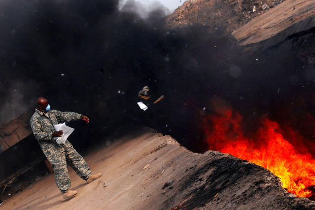 An Air Force master sergeant tosses unserviceable uniform items into a burn pit at Balad Air Base, Iraq on March 10, 2008. (US Air Force photo/Julianne Showalter)