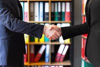 Two people wearing suits shake hands. (Stock image)